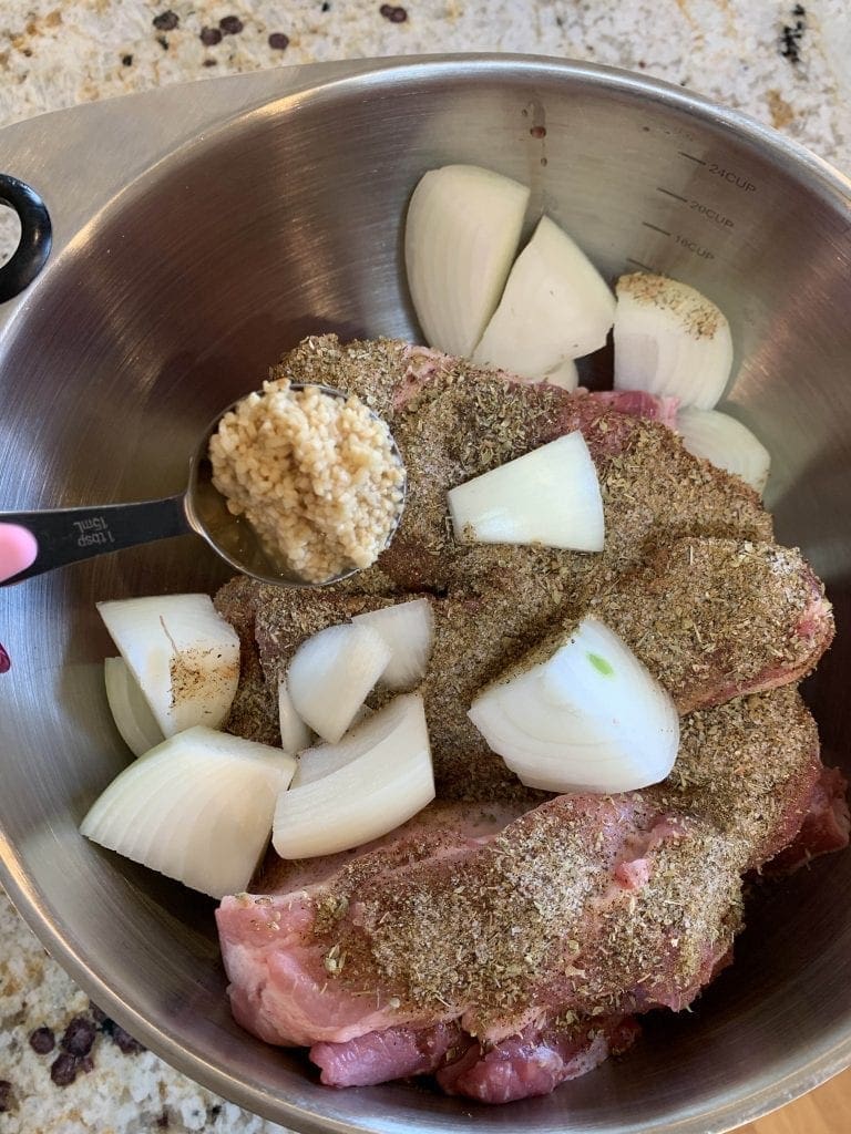 garlic being added to a bowl of onions and seasoned meat