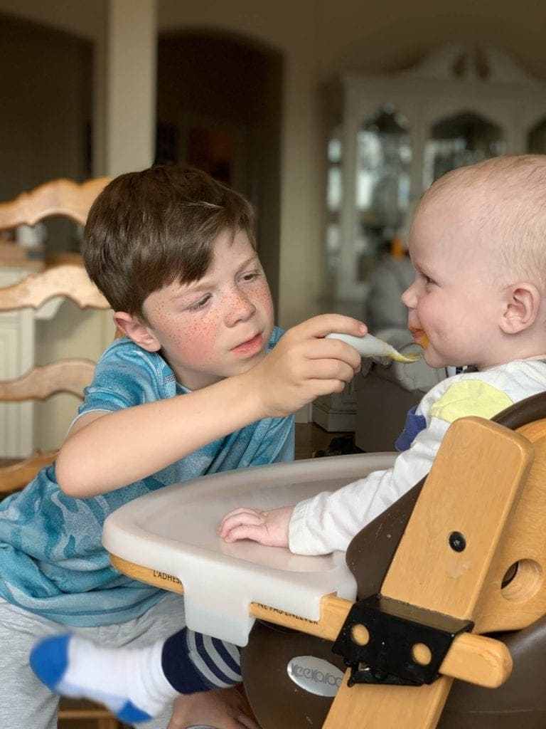 Brother feeding his baby brother in a high chair in the kitchen
