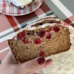 Slice of brown quick bread with red cranberries and white glaze on top