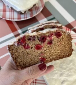 Slice of brown quick bread with red cranberries and white glaze on top