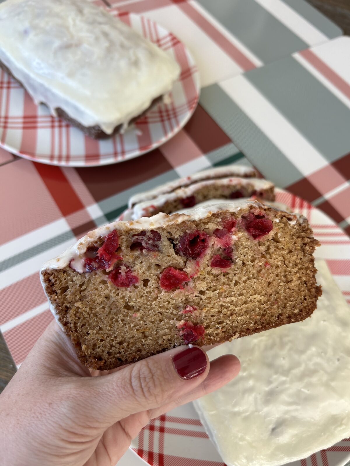 A slice of brown quick bread with red cranberries and white glaze topping.
