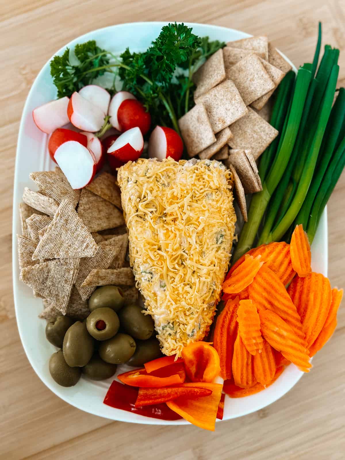 Cheese ball shaped like a carrot on a platter with veggies and crackers