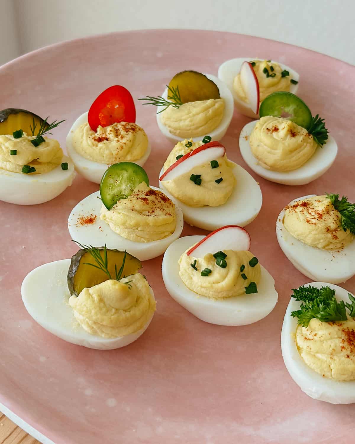 deviled eggs with pickles and radish slices, parsley and peppers on a pink plate