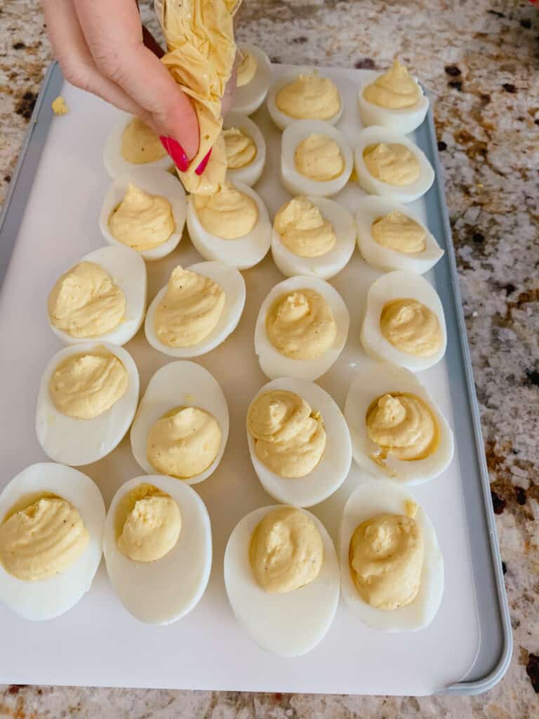 deviled eggs lined up on a cutting board being fulled with a ziplock bag full of yolk mixture