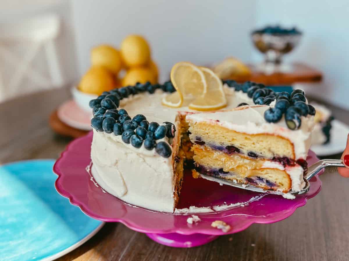 Whole layered cake with blueberries with a spatula holding one slice