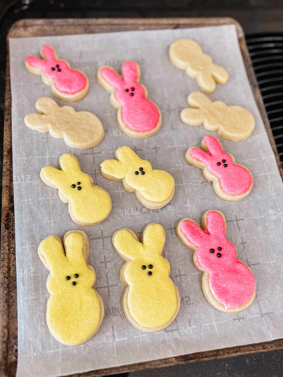 partially decorated yellow and pink peeps sugar cookies on a baking sheet lined with parchment paper