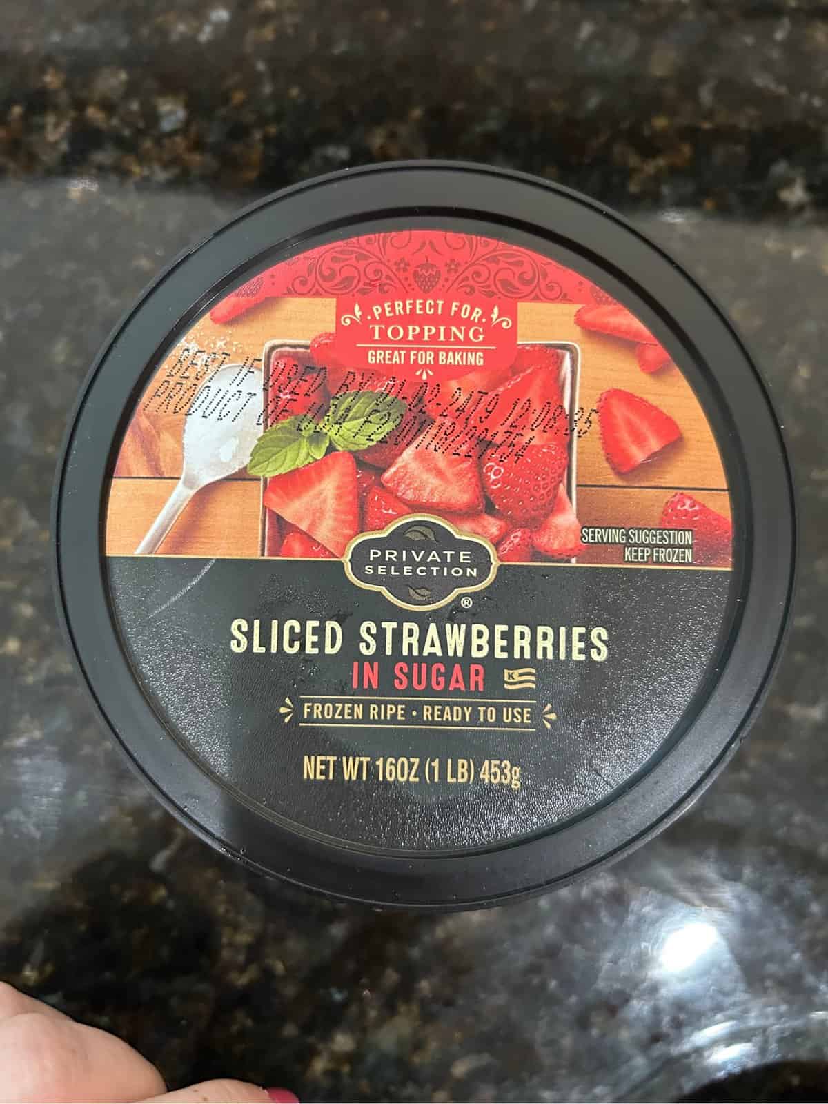 Grocery store brand container of frozen sliced strawberries, Black lid with red berries