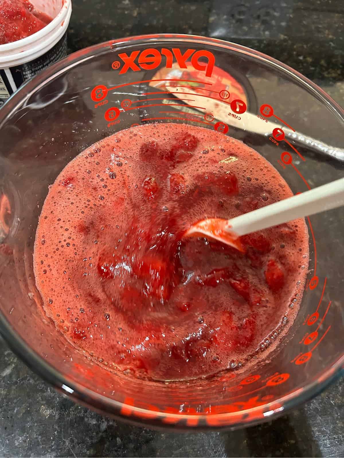 Glass measuring cup with strawberry jello and a white spatula