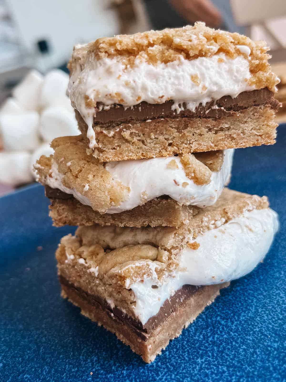 3 cookie bars stacked on a blue plate with a layer of gooey marshmallow fluff and chocolate