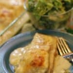 Cheese covered enchilada on a blue plate with a fork and sour cream