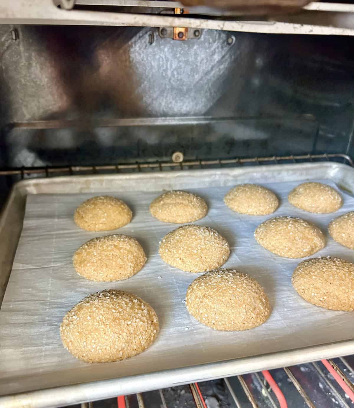 ginger molasses cookies on a baking sheet in the oven slightly puffed up