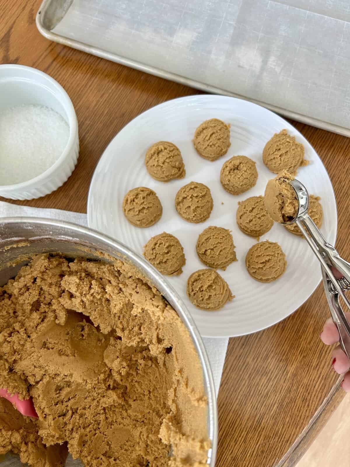 cookie dough in a silver mixing bowl and cookie dough balls on a white plate with a cookie scoop