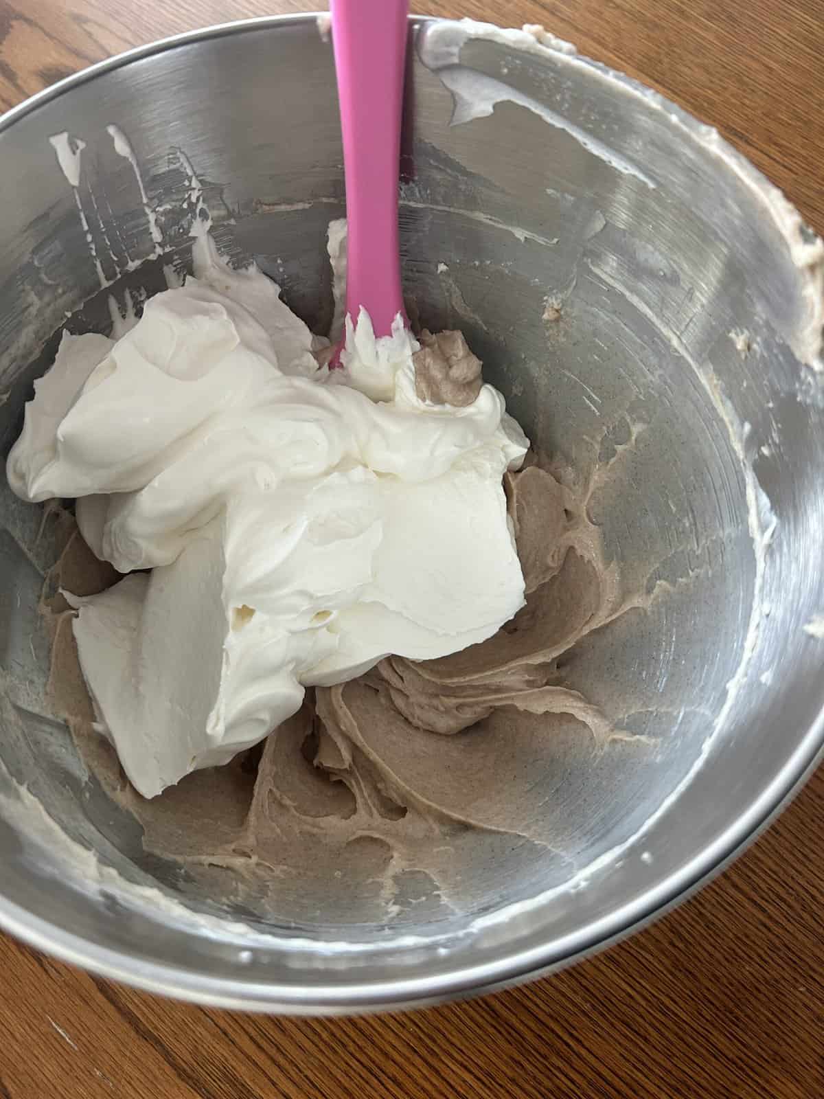 Cinnamon and sugar cream cheese smooth in a mixing bowl with fluffy whipped cream added on top